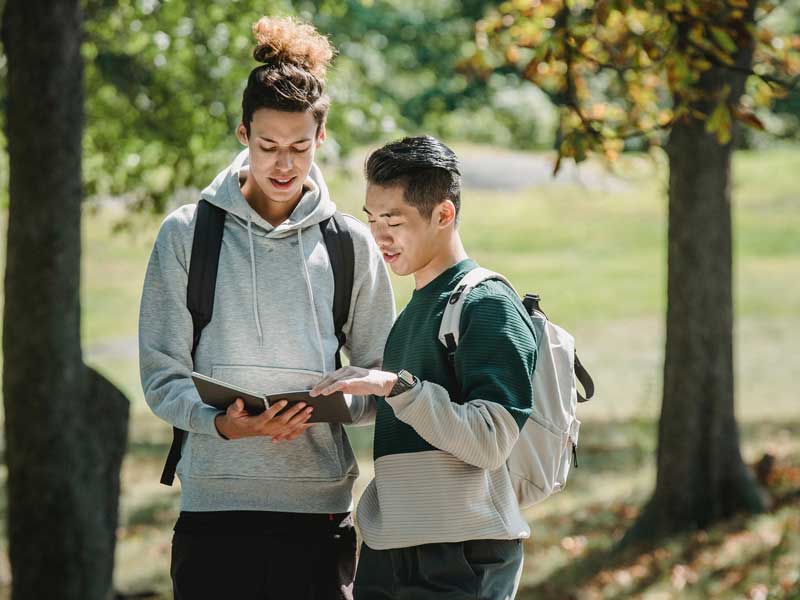 two students looking at a notebook together in a park