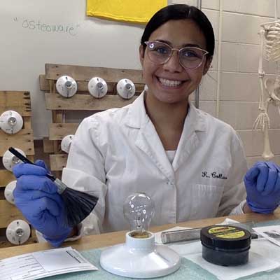 a student in a lab coat practicing dusting a lightbulb for fingerprints