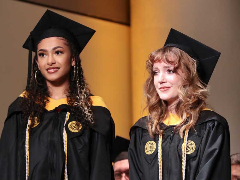 two v.c.u. graduates on stage dressed in commencement regalia