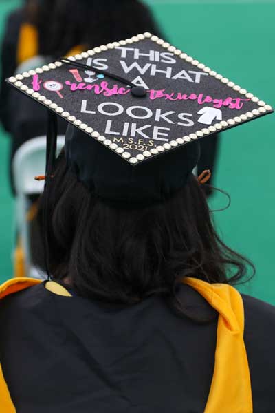 a v.c.u. student dressed in commencement regalia at a graduation ceremony. her mortarboard reads 'this is what a forensic toxicologist looks like'