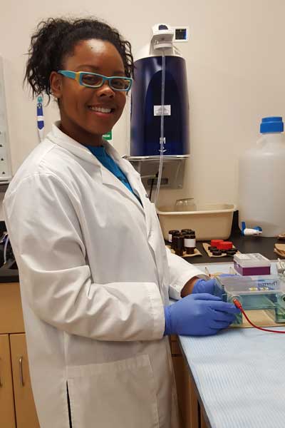 a smiling student lab worker working with a piece of lab equipment