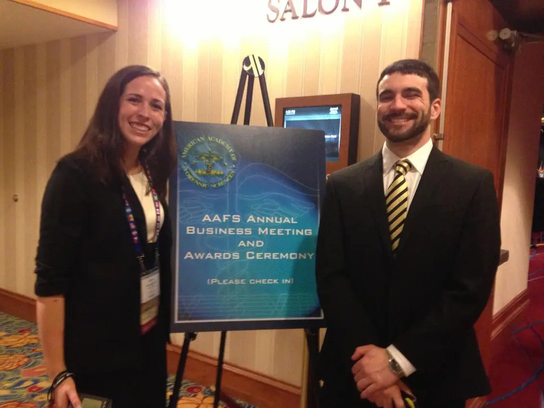 Two people in business attire stand in front of an easel at an event