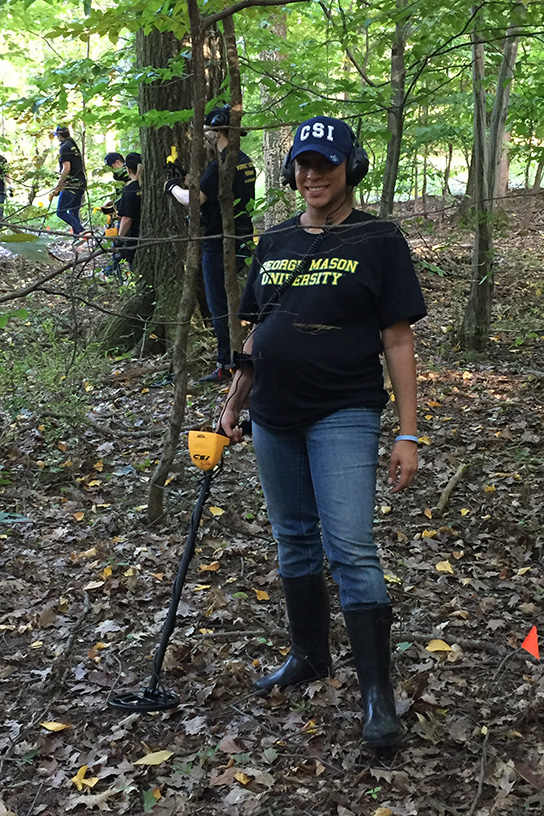 Kelly Knight stands in the woods holding a metal detector